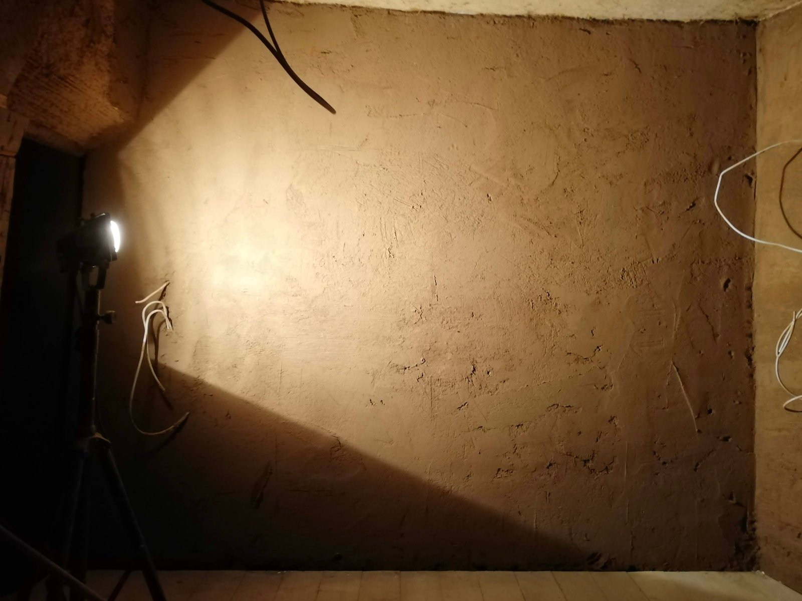 Lehmputz auf Innenwand im Nachtlicht, Fachwerkbalken sichtbar, Zwischenstand Sanierung