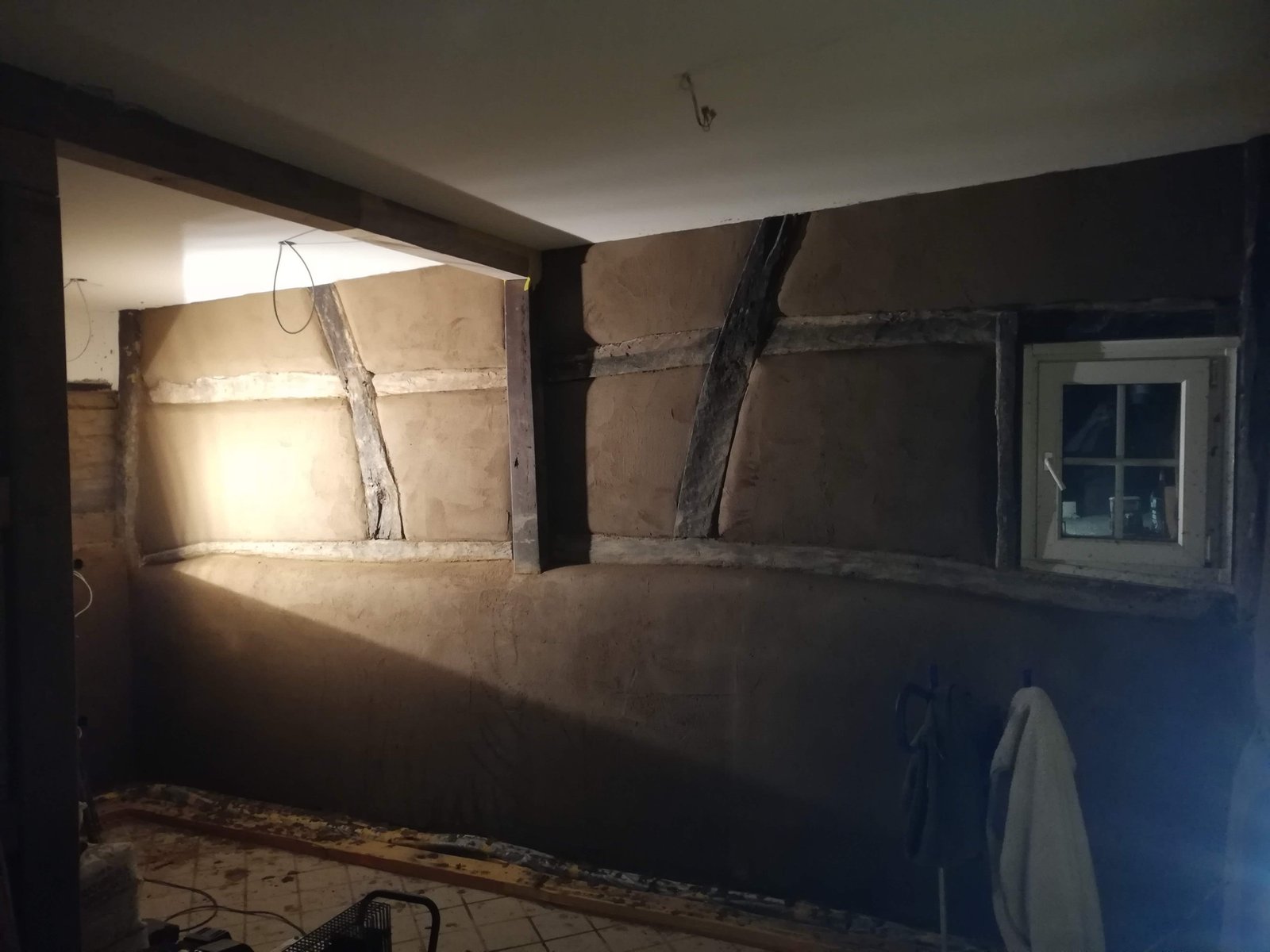 Frischer Lehmputz auf Wandfläche im Dunkeln, glatte Oberfläche nach Auftrag