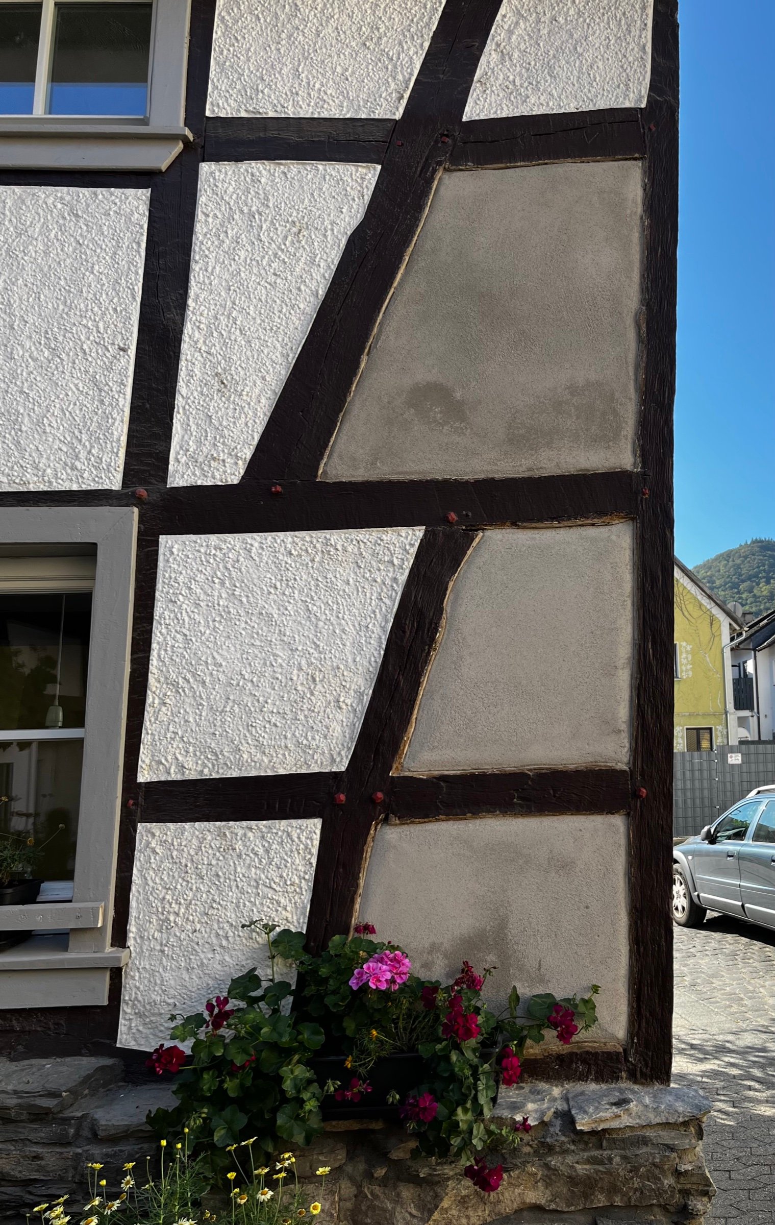 Fachwerkfassadendetail: neue weiße Putzgefache, schwarze Holzbalken, blaues Fenster