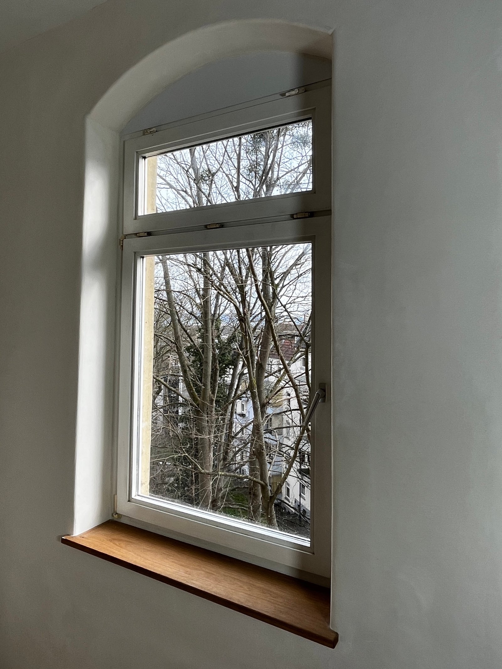 Sanierter Altbau-Raum: neugotisches Rundbogenfenster mit weißem Kalkputz eingerahmt