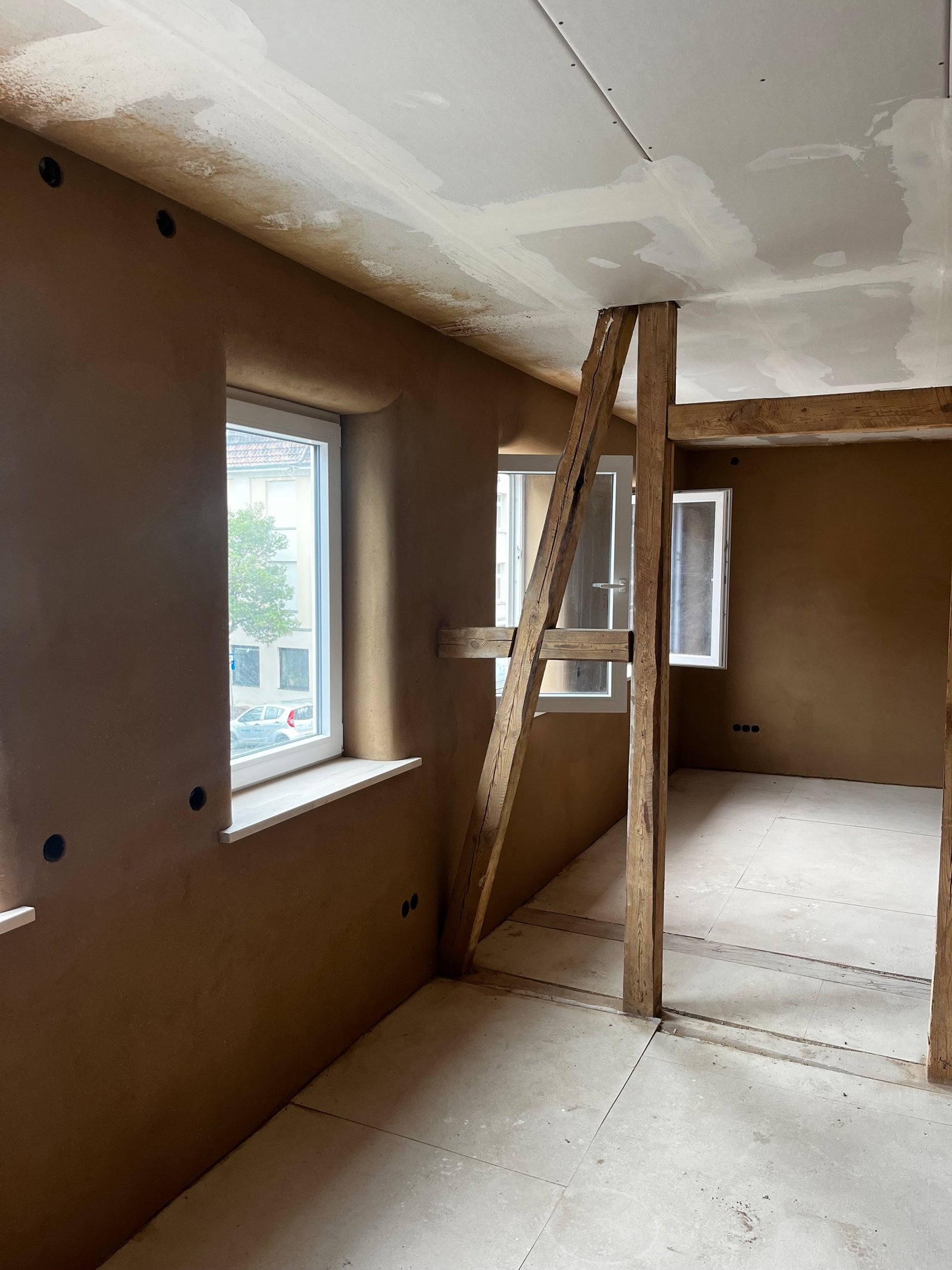 Lehmputz-Innenwand im Treppenhaus, warmer Braunton, sichtbarer Holzbalken, fertig