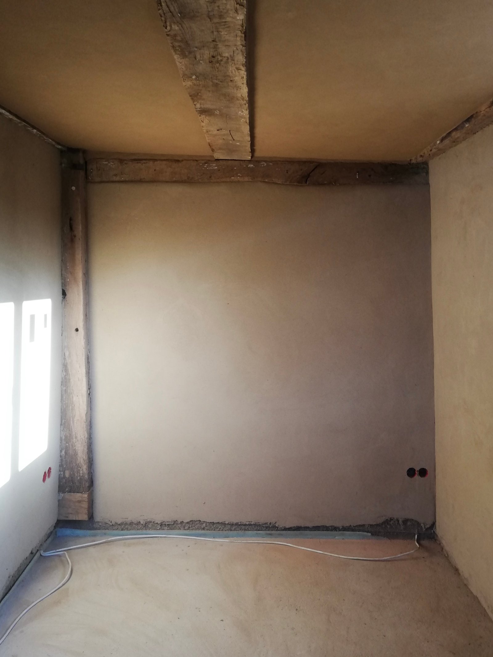 Frischer Lehmputz auf Innenwand, Fachwerkbalken sichtbar, Sanierungsphase Niedersachsen