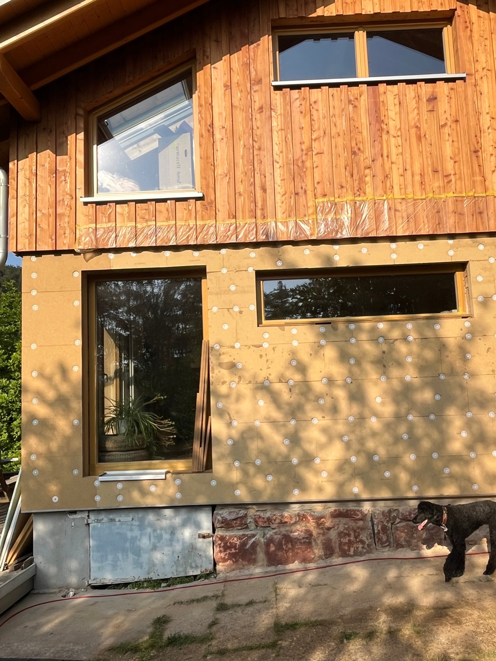 Hütte im Wald: Holzfassade mit angebrachten Holzfaserdämmplatten, Eingang sichtbar