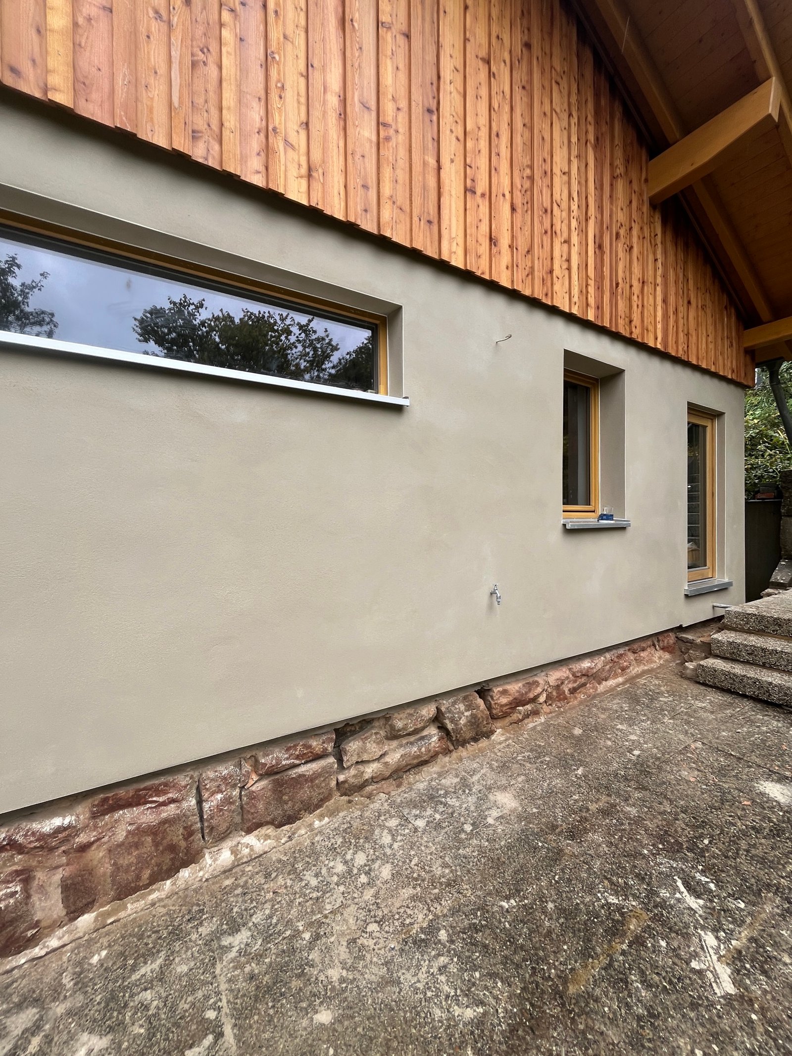 Fertiggestellte Fassade Gesamtansicht: Kalkputz unten, Holzschalung oben, Holzdach