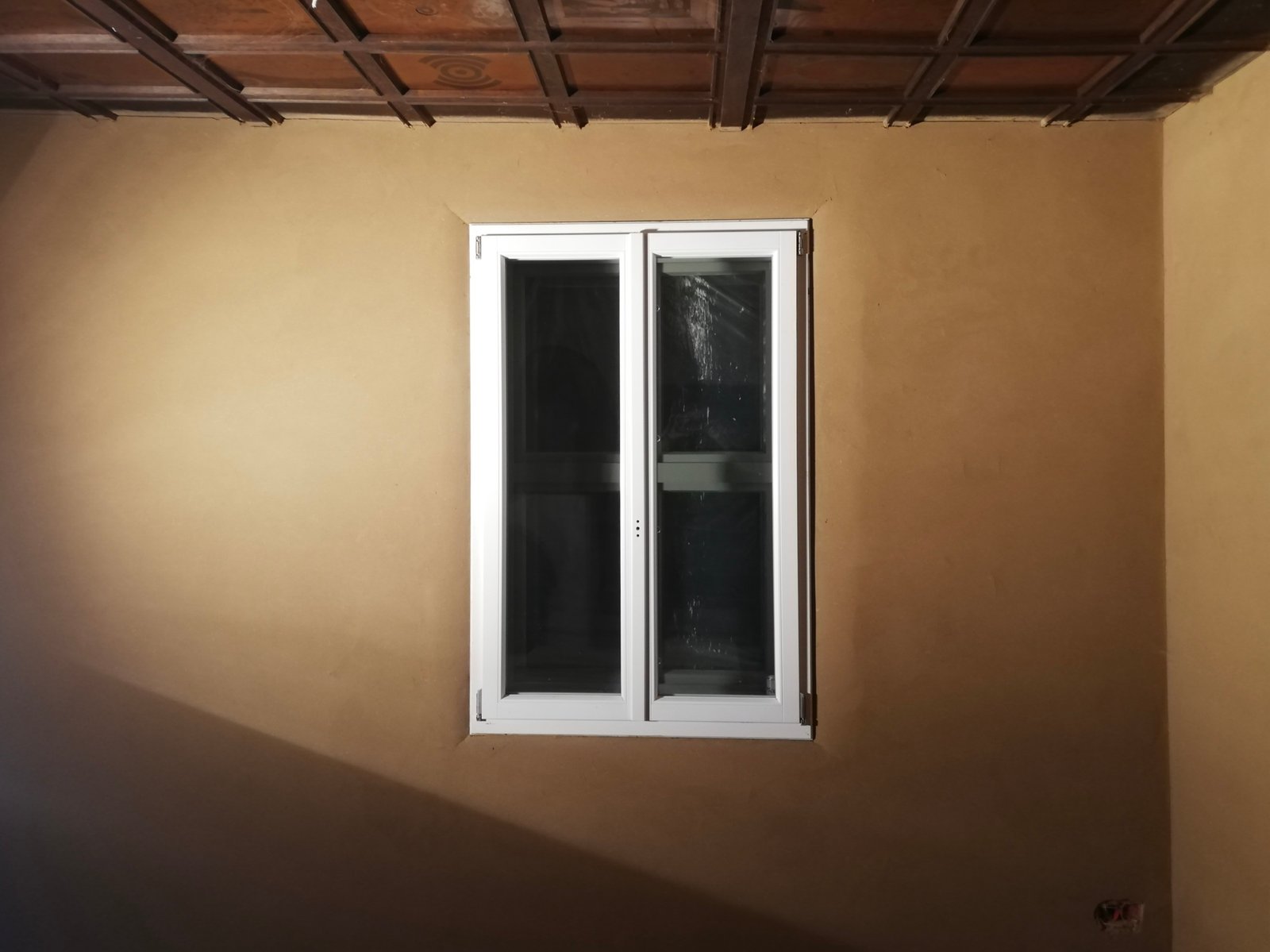 Lehmputzwand mit historischem Holzbalken und kleiner Fensteröffnung, Detailansicht