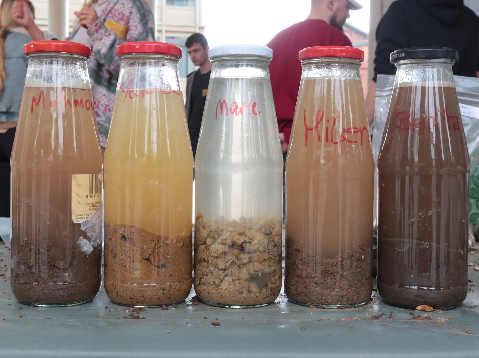 Lehm-Workshop: fünf beschriftete Flaschen mit Bodenproben verschiedener Teilnehmer