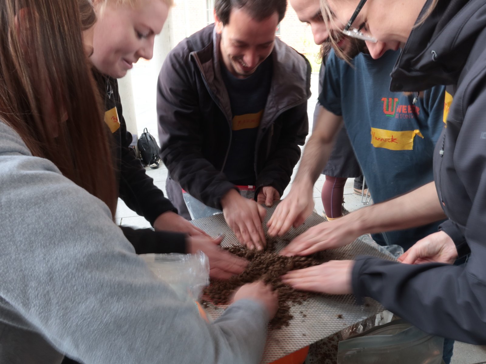 Lehm-Workshop: Studierende kneten gemeinsam Lehmgemisch auf Sieb