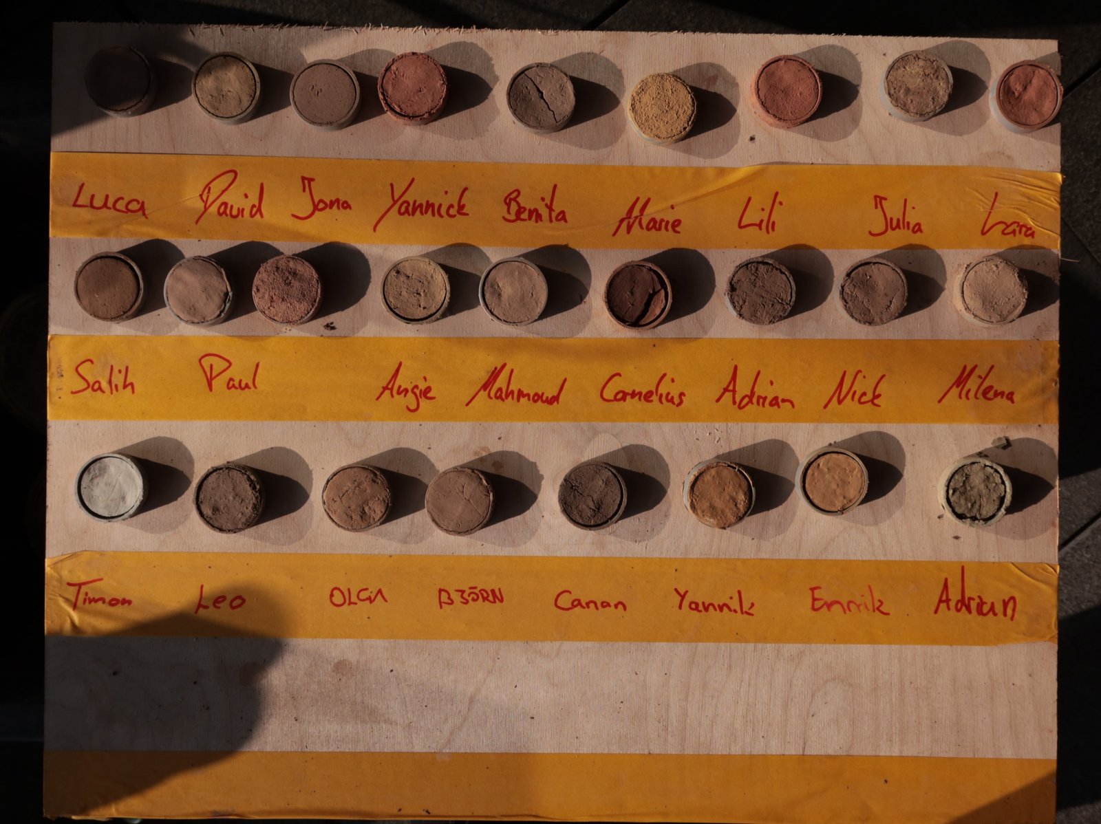 Lehmproben-Farbpalette: 24 Lehmproben auf Holzbrett mit Teilnehmernamen