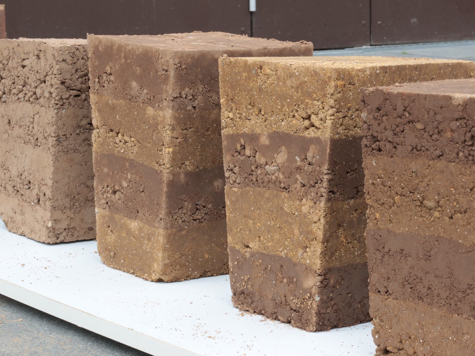Stampflehmproben: drei Lehmblöcke mit sichtbaren Schichtlagen nebeneinander