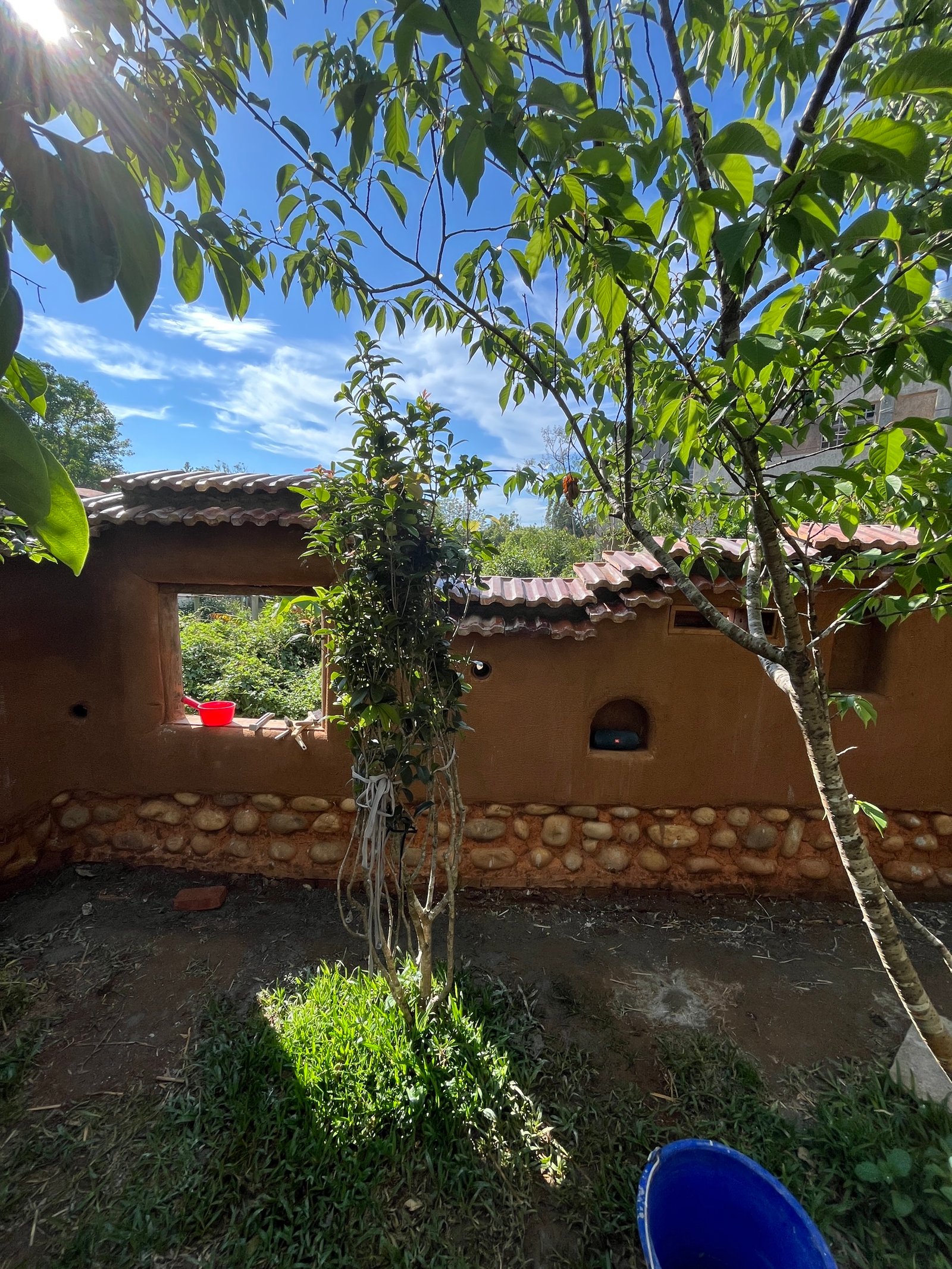 Lehmbauprojekt Taiwan: Außenansicht mit Dachziegeln, Flusssteinband, blaue Plane
