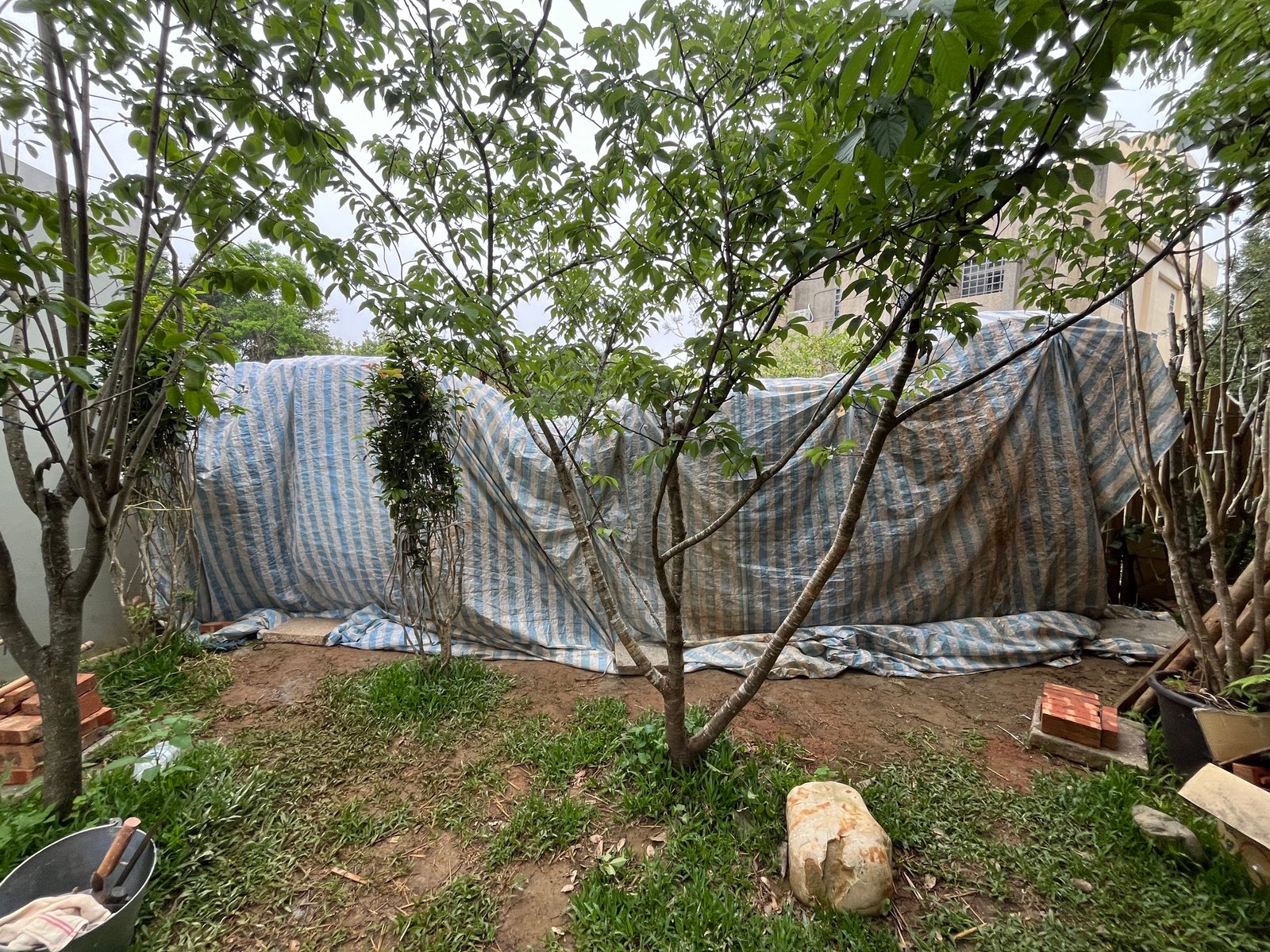 Lehmbaustelle Taiwan: Wandaufbau unter blauer Schutzplane im Garten