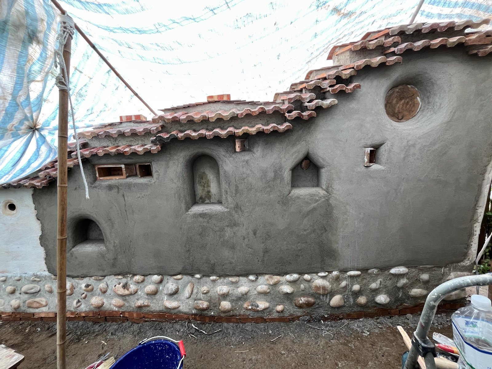 Stampflehm-Wandoberfläche mit skulptierten Wandnischen und Dachziegelabdeckung