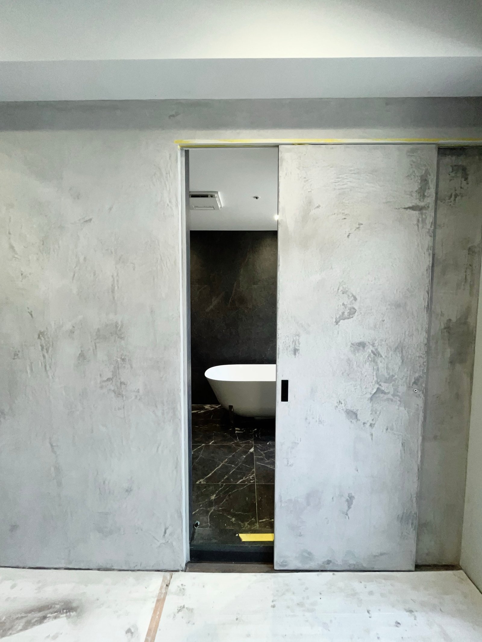 Kalkputzwand mit Badtür: grau-weiße Oberfläche, freistehende Badewanne sichtbar